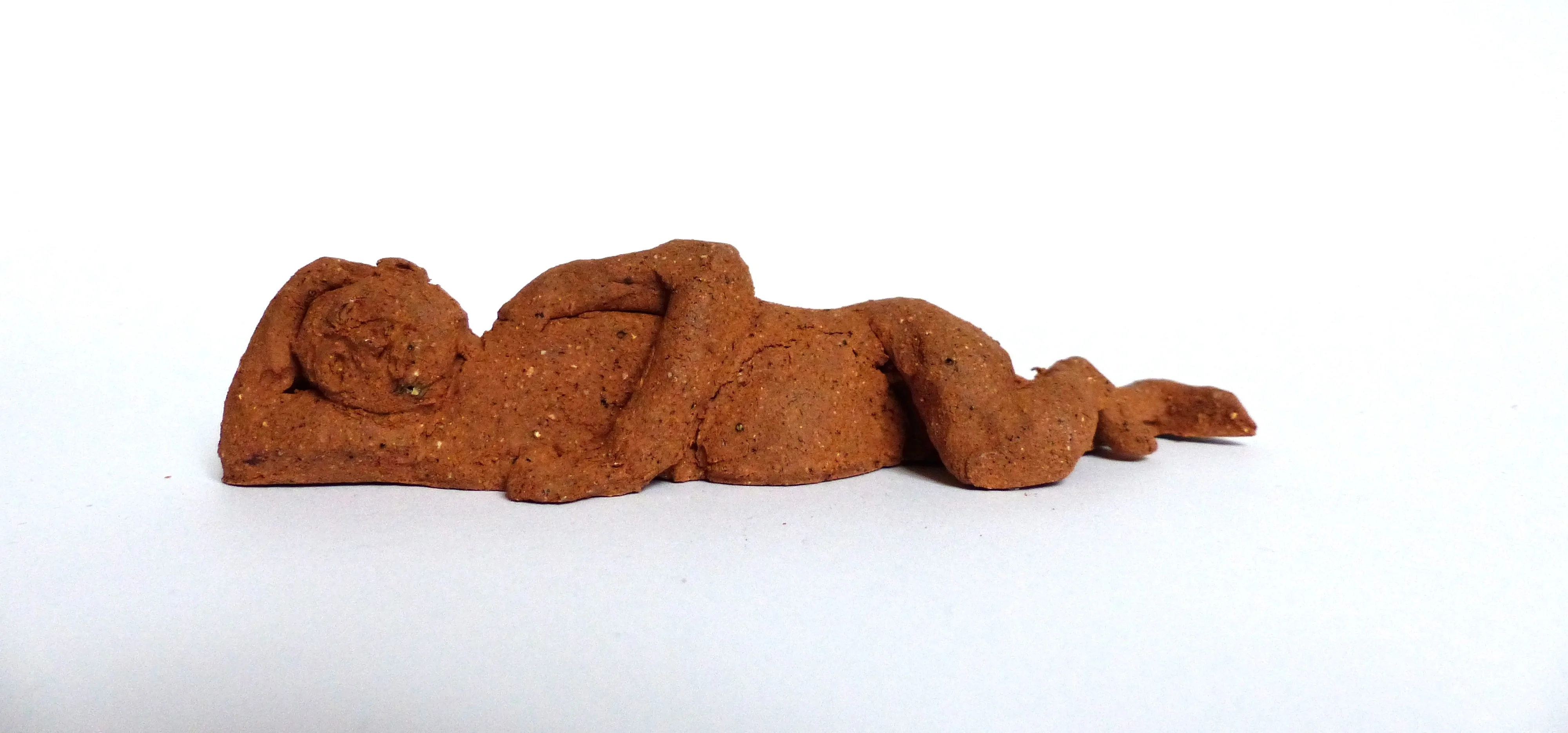 Sculpture d'une personne allongée sur son flanc droit en terre collectée, nue